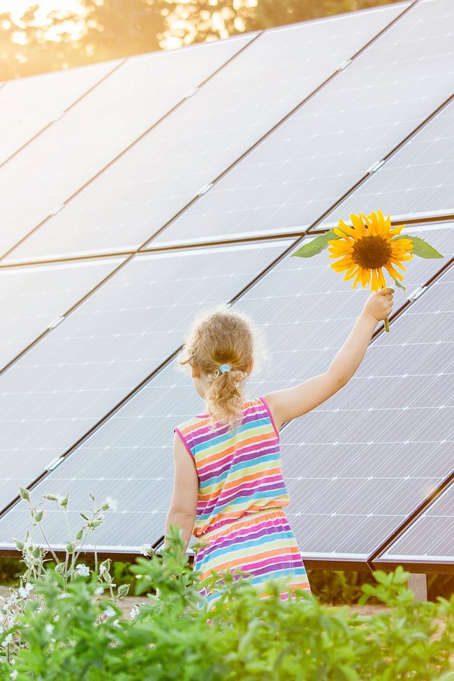 1812515899 Kleines Mädchen mit Sonnenblume vor PV-Anlage